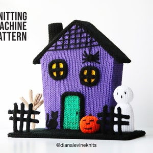Pode incluir: Padrão de máquina de tricô para uma casa de Halloween roxa com uma porta verde, um gato preto, uma teia de aranha e um fantasma. A casa é cercada por uma cerca preta e uma árvore nua.