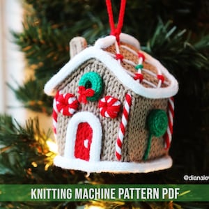 May include: Knitting machine pattern PDF for a gingerbread house ornament. The ornament is brown with white icing and red candy canes. It has a green wreath on the front and a red door.