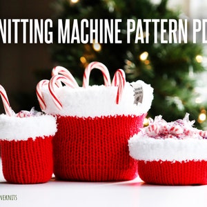 Pode incluir: Três cestas de malha vermelha com guarnição de pele sintética branca, cheias de bengalas de caramelo e doces embrulhados. As cestas estão sobre uma superfície branca em frente a uma árvore de Natal desfocada.