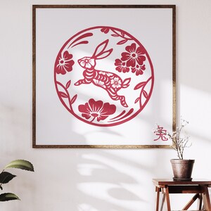 May include: A framed print featuring a red paper-cut design of a rabbit within a floral circle. The artwork, set against a white background, includes the Chinese character for rabbit. The frame is a warm brown, and the overall aesthetic is a celebration of the Lunar New Year.