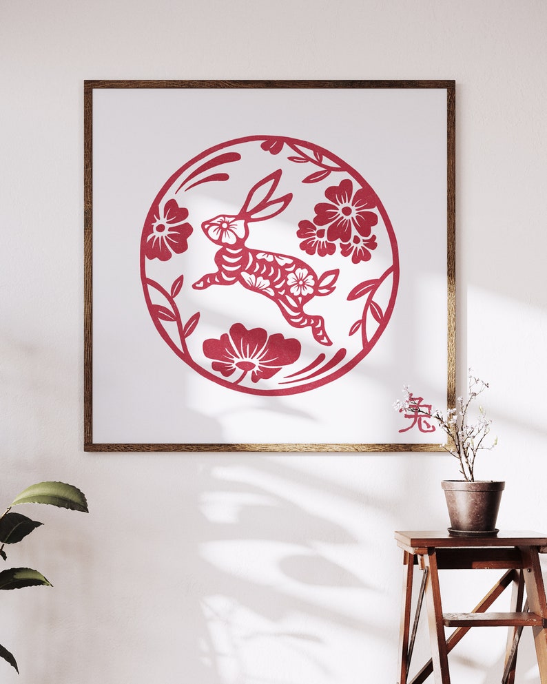 May include: A framed print featuring a red paper-cut design of a rabbit within a floral circle. The artwork, set against a white background, includes the Chinese character for rabbit. The frame is a warm brown, and the overall aesthetic is a celebration of the Lunar New Year.