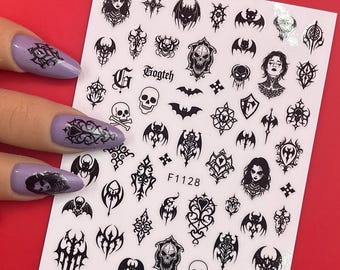 May include: Sheet of black nail art stickers with gothic-themed designs, including skulls, bats, and portraits of women. The sheet is held against a red background. The text "F1128" is printed on the sheet.