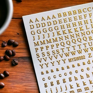 May include: A white sheet with gold letters of the alphabet, A through Z, in a repeating pattern. The letters are arranged in rows and columns. The sheet is labeled "MYSW002".