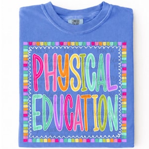 May include: A periwinkle blue t-shirt featuring a rectangular frame with a multicolored scalloped border. Inside the frame, the text "PHYSICAL EDUCATION" is written in large, vibrant, multi-colored bubble letters against a blue background.