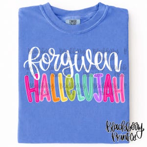 May include: A blue t-shirt with the words "forgiven" in white script above the word "hallelujah" in colorful block letters. The shirt has a tag that says "Comfort Colors" and a logo that says "Blackberry Print Co."