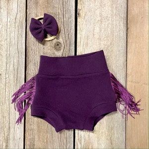 May include: Purple baby shorts with a ruffled trim and a matching purple bow headband.