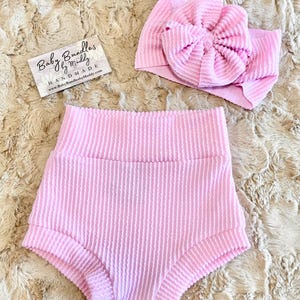 Peut inclure: Un short rose pour bébé avec un bandeau assorti rose. Le bandeau est fait d'un tissu doux et extensible et a un grand nœud. Le short est fait d'un tissu côtelé et a une coupe confortable.