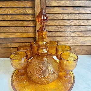 May include: Amber glass decanter with a floral design and six matching glasses on a matching tray. The set is perfect for serving drinks.