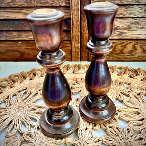 May include: Two wooden candle holders with a dark brown finish. The candle holders are on a woven straw placemat.