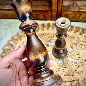 May include: Two wooden candle holders with a dark brown finish. The candle holders are made of wood and have a simple design. They are perfect for adding a touch of rustic charm to any home.