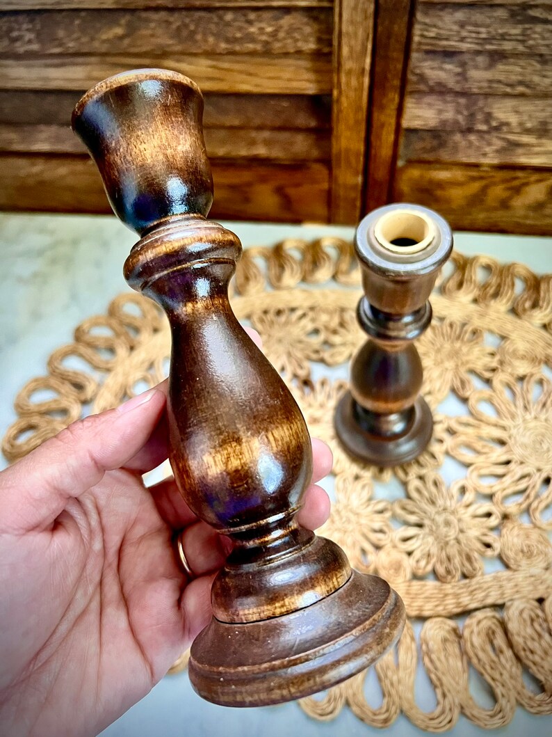 May include: Two wooden candle holders with a dark brown finish. The candle holders are made of wood and have a simple design. They are perfect for adding a touch of rustic charm to any home.