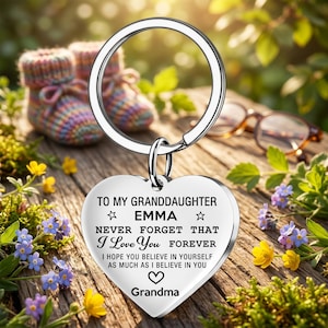 May include: A silver-toned heart-shaped keychain with a metal ring. The front is engraved with the text: TO MY GRANDDAUGHTER EMMA NEVER FORGET THAT I Love You FOREVER I HOPE YOU BELIEVE IN YOURSELF AS MUCH AS I BELIEVE IN YOU, with a heart icon and Grandma.