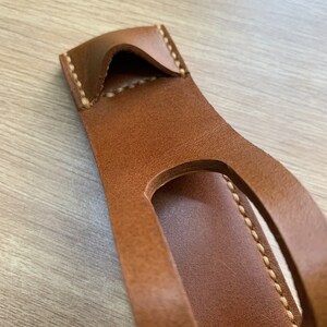 May include: A brown leather phone case with a cut-out for the camera lens and a stitched edge.