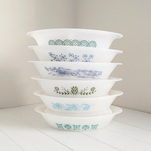 May include: A stack of six white oval-shaped bowls with blue and green floral patterns. The bowls are stacked in a pyramid shape.