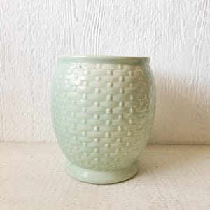 May include: A light green ceramic planter with a woven pattern. The planter is round and has a wide base.