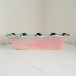 May include: A rectangular ceramic planter with a wavy rim and a pink and green glaze. The planter has a subtle wave pattern.