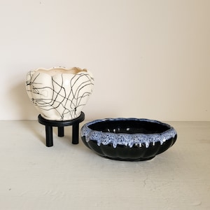 May include: Two ceramic planters, one white with black lines and one black with blue glaze. The white planter is on a black stand.