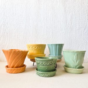 May include: Five vintage ceramic plant pots in different colors and designs. The pots are arranged in a row on a white surface. The pots are all in good condition and have a classic look.