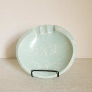 May include: A light blue ceramic ashtray with a white marbled design. The ashtray is round and has a slightly raised edge.
