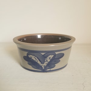 May include: A small, round, gray ceramic bowl with a blue and white heart design. The bowl is glazed and has a brown interior.