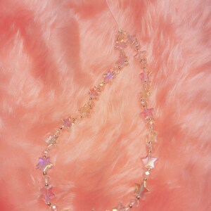 May include: A clear iridescent star-shaped beaded phone charm on a pink fuzzy background.