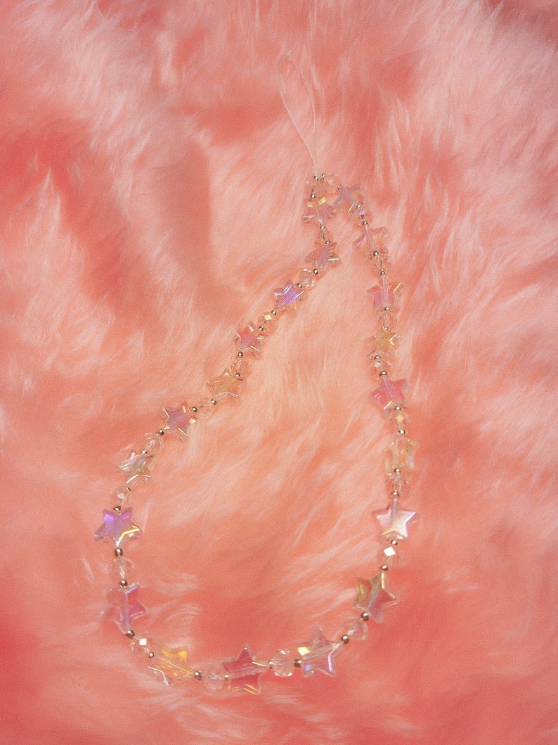 May include: A clear iridescent star-shaped beaded phone charm on a pink fuzzy background.