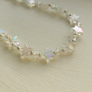 May include: A delicate iridescent star-shaped bead necklace with clear beads. The necklace is made of silver and has a subtle shimmer.