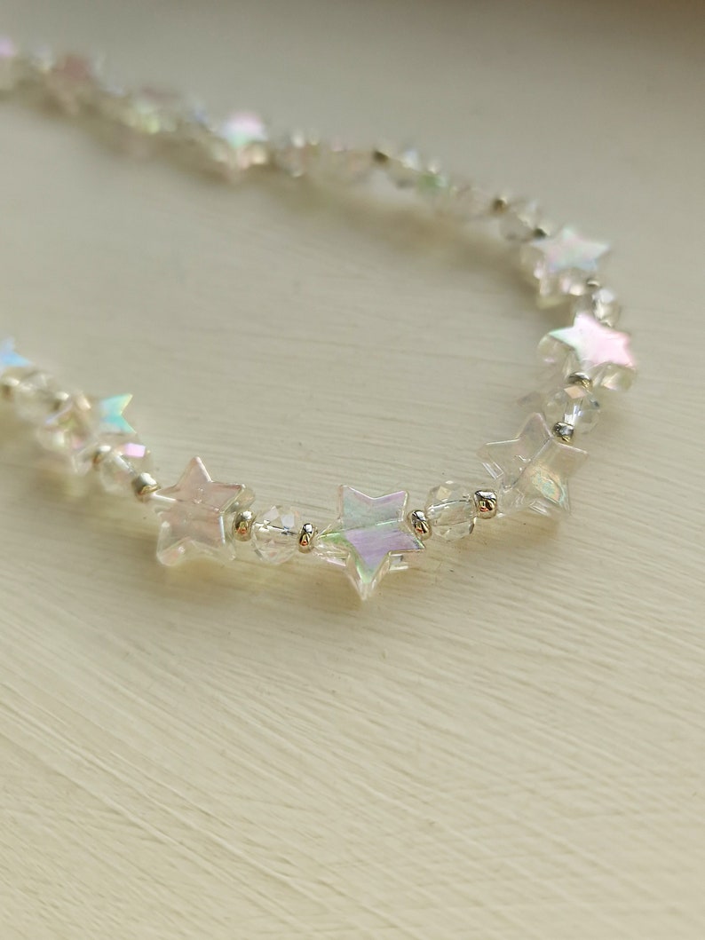 May include: A delicate iridescent star-shaped bead necklace with clear beads. The necklace is made of silver and has a subtle shimmer.