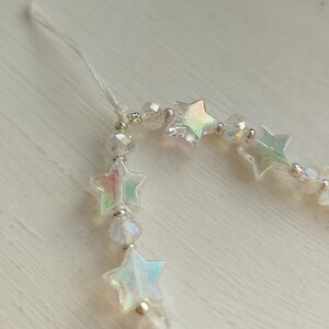 May include: A white string with iridescent star-shaped beads and clear crystal beads.