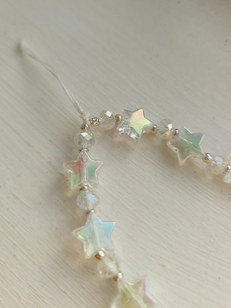 May include: A white string with iridescent star-shaped beads and clear crystal beads.