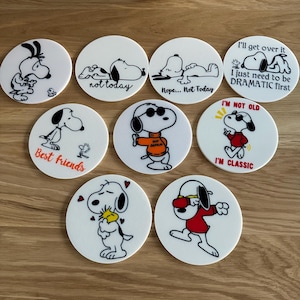 May include: Set of 8 round white coasters featuring black and white illustrations of Snoopy with various quotes. The quotes include "not today", "Nope... Not Today", "Best friends", "I'll get over it I just need to be DRAMATIC first", "I'M NOT OLD", and "I'M CLASSIC".