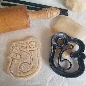 May include: A close-up of two cookie cutters, one is a plain cookie dough and the other is a black metal cookie cutter in the shape of the number 5.