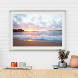 Peut inclure: Une photographie encadr&eacute;e d'une sc&egrave;ne de plage avec un coucher de soleil sur l'oc&eacute;an. La photo montre une plage de sable avec des vagues qui se brisent sur le rivage. Le ciel est un m&eacute;lange de rose, d'orange et de violet.
