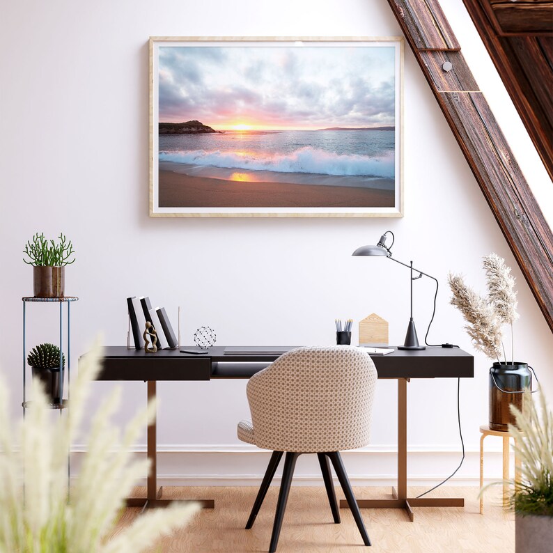 Peut inclure: Une photographie encadr&eacute;e d'une sc&egrave;ne de plage avec un coucher de soleil sur l'oc&eacute;an. La photo est accroch&eacute;e &agrave; un mur blanc au-dessus d'un bureau noir avec une chaise blanche. Il y a des plantes sur une &eacute;tag&egrave;re &agrave; gauche du bureau.