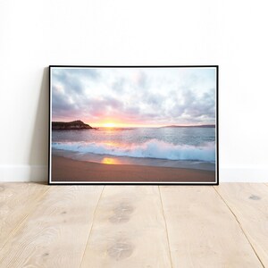 Peut inclure: Une photographie d'une sc&egrave;ne de plage avec un coucher de soleil en arri&egrave;re-plan. Les vagues se brisent sur le rivage et le sable est d'une couleur dor&eacute;e claire. Le ciel est un m&eacute;lange de rose, d'orange et de bleu.