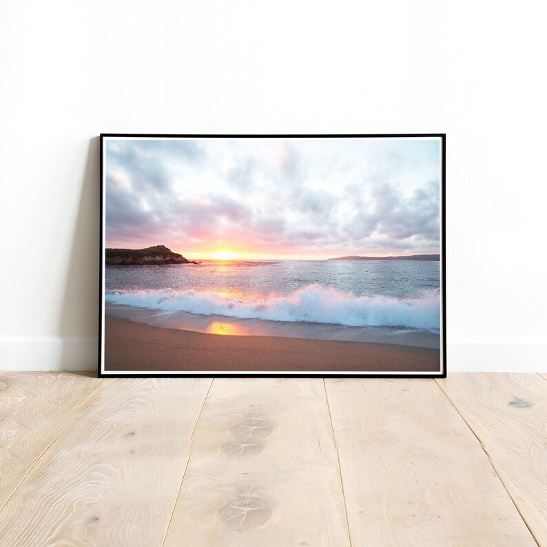 Peut inclure: Une photographie d'une sc&egrave;ne de plage avec un coucher de soleil en arri&egrave;re-plan. Les vagues se brisent sur le rivage et le sable est d'une couleur dor&eacute;e claire. Le ciel est un m&eacute;lange de rose, d'orange et de bleu.