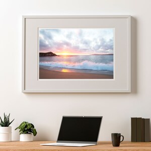 Peut inclure: Une photographie encadr&eacute;e d'une sc&egrave;ne de plage avec un coucher de soleil sur l'oc&eacute;an. La photo montre une plage de sable avec des vagues qui se brisent sur le rivage. Le ciel est un m&eacute;lange de rose, d'orange et de bleu.