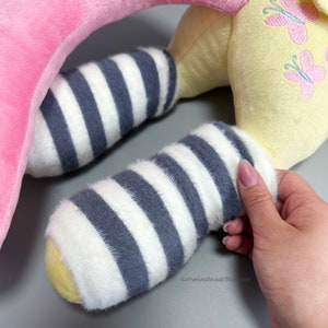 May include: A yellow plush toy with pink butterfly embroidery and gray and white striped legs. The toy is shaped like a horse with a pink head and neck.