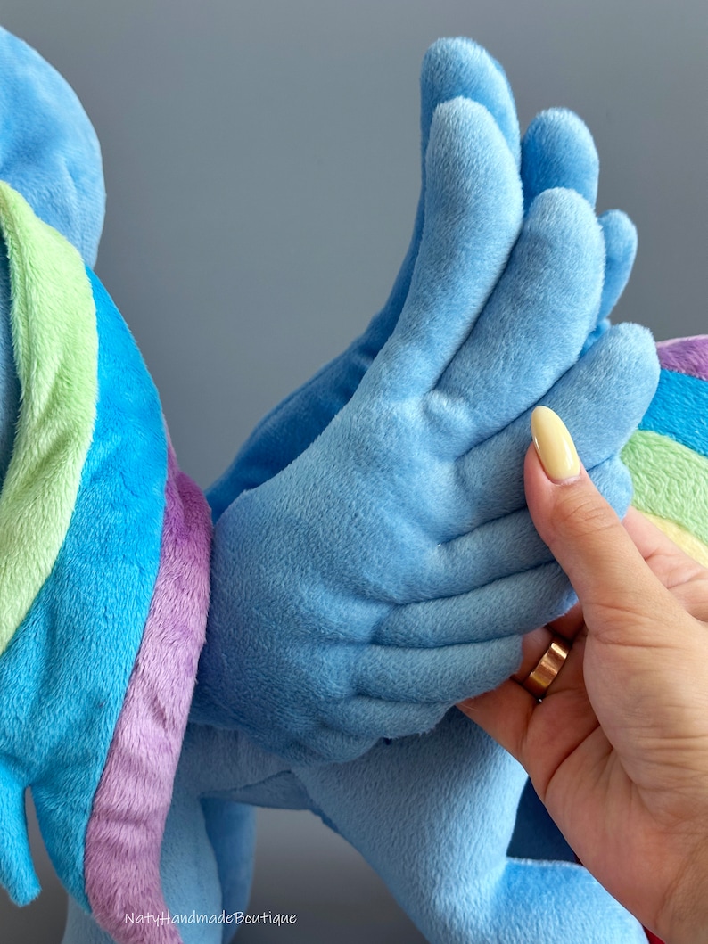 May include: A plush toy of a blue and purple unicorn with a rainbow mane and tail. The unicorn has large, blue wings with a soft, fuzzy texture.