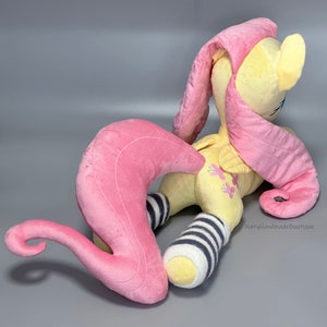 May include: A plush toy of Pinkie Pie from My Little Pony, with a yellow body, pink mane and tail, and black and white striped socks. The toy is lying on its side with its head turned to the side.