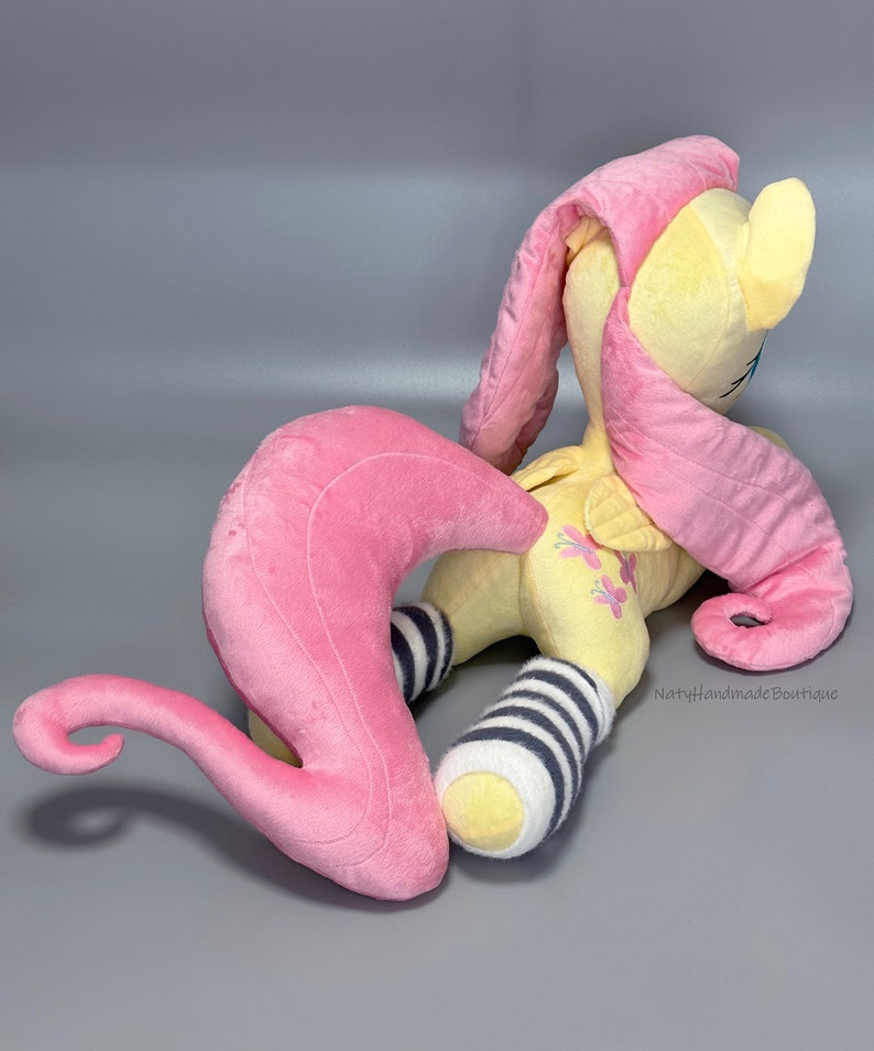May include: A plush toy of Pinkie Pie from My Little Pony, with a yellow body, pink mane and tail, and black and white striped socks. The toy is lying on its side with its head turned to the side.