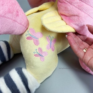 May include: A plush toy with pink and yellow fur, a striped leg, and embroidered pink butterflies on the back. The toy is made by NattyHandmade.