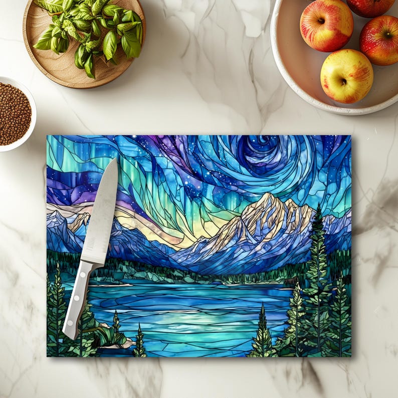 May include: Rectangular cutting board with a stained glass design depicting a mountain landscape with a lake and evergreen trees. The color palette includes blues, greens, and purples. A stainless steel knife rests on the board.