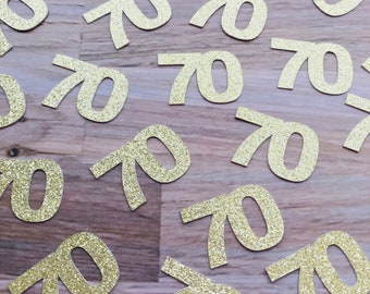 May include: Gold glitter confetti with the number 70 printed on each piece. The confetti is scattered on a wooden surface.