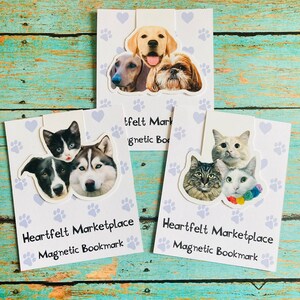May include: Three magnetic bookmarks featuring images of dogs and cats. Each bookmark has a different arrangement of pet faces, with paw prints and hearts in the background. The text "Heartfelt Marketplace Magnetic Bookmark" is printed on each bookmark.