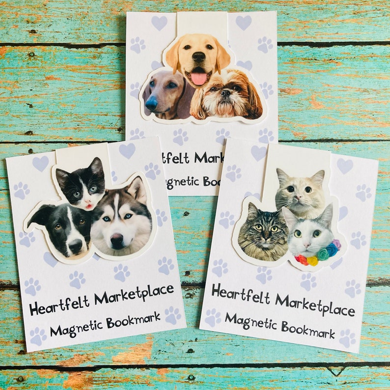 May include: Three magnetic bookmarks featuring images of dogs and cats. Each bookmark has a different arrangement of pet faces, with paw prints and hearts in the background. The text "Heartfelt Marketplace Magnetic Bookmark" is printed on each bookmark.