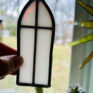 May include: A white stained glass window ornament with a black frame and a gothic arch design.