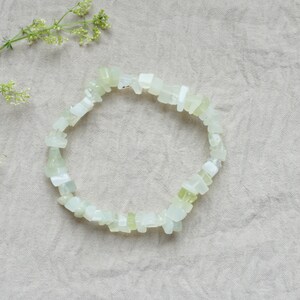 Könnte beinhalten: Ein Armband aus weißem Jade-Stein mit einem hellgrünen Farbton. Das Armband besteht aus kleinen, unregelmäßig geformten Steinen.