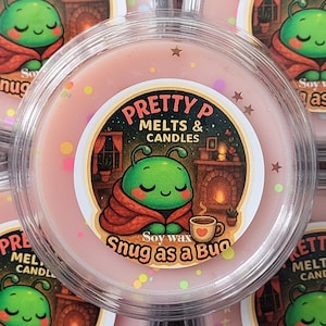 May include: A circular, pink soy wax melt in a clear plastic container. The label says "PRETTY P MELTS & CANDLES" and shows a cartoon bug in a blanket with a coffee cup. The text "Snug as a Bug" is also on the label.