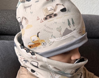 May include: A beige knitted hat and matching neck warmer with a pattern of construction vehicles and trees. The hat has a grey brim.